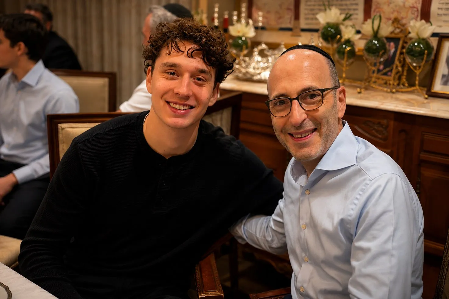 A student and an executive seated together at a Shabbat table, both smiling